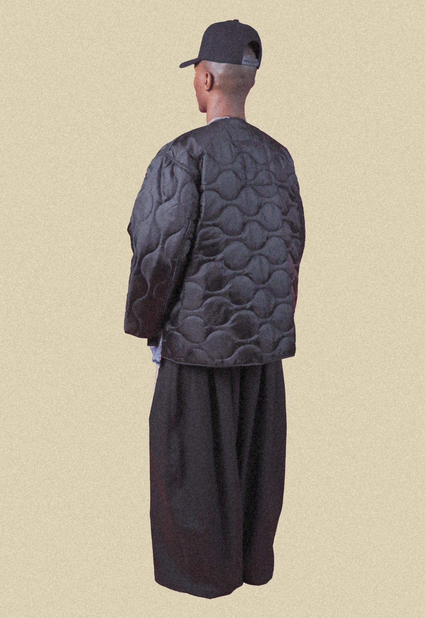 Man wearing coated black denim wide-leg trousers, repurposed vintage denim bomber on a beige background