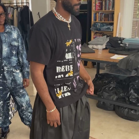 Man wearing coated black denim double waistband wide-leg trousers and black t-shirt in an apparel design studio atelier.