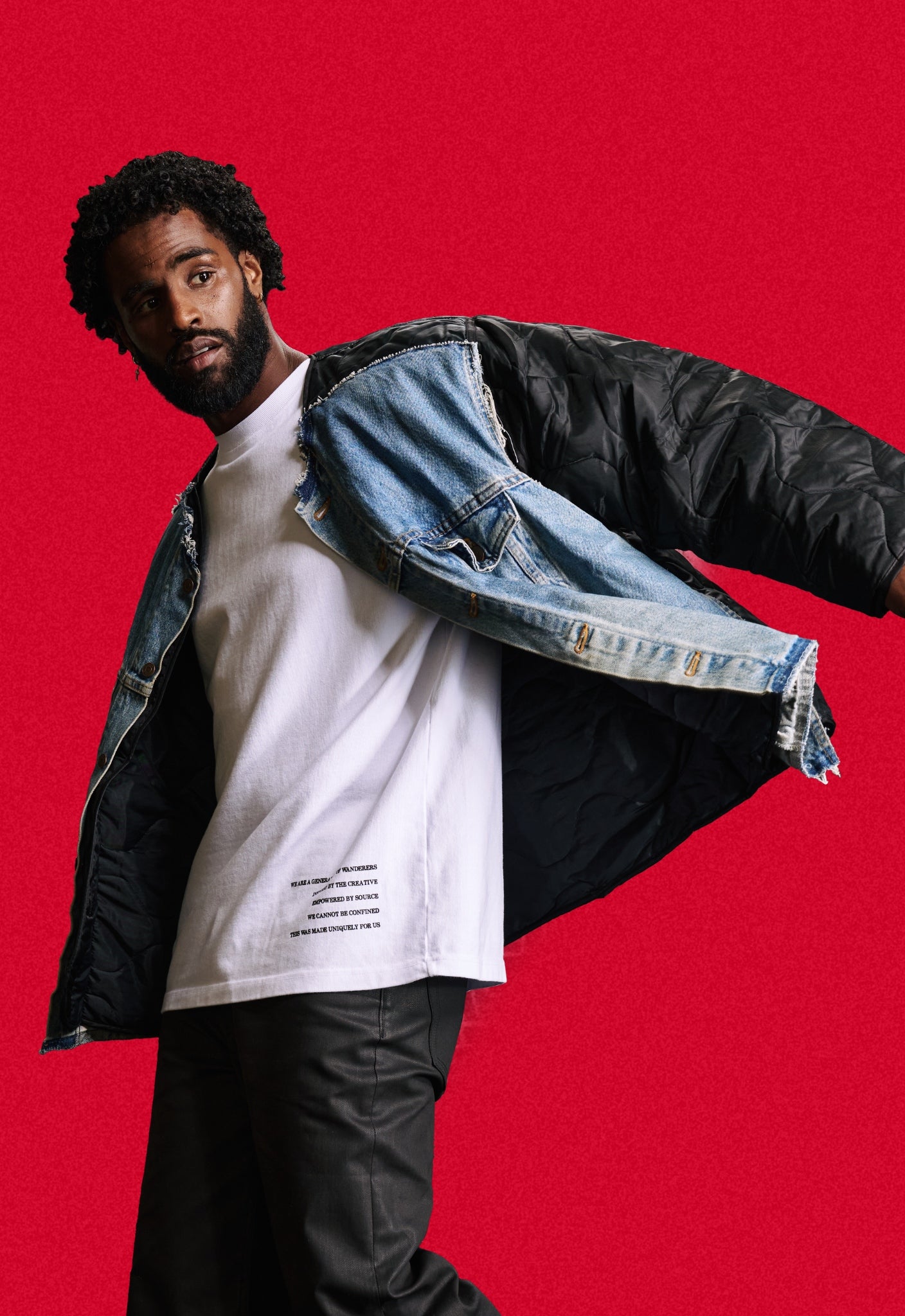 Man wearing a black quilted repurposed denim jacket over a heavyweight white t-shirt on a red background