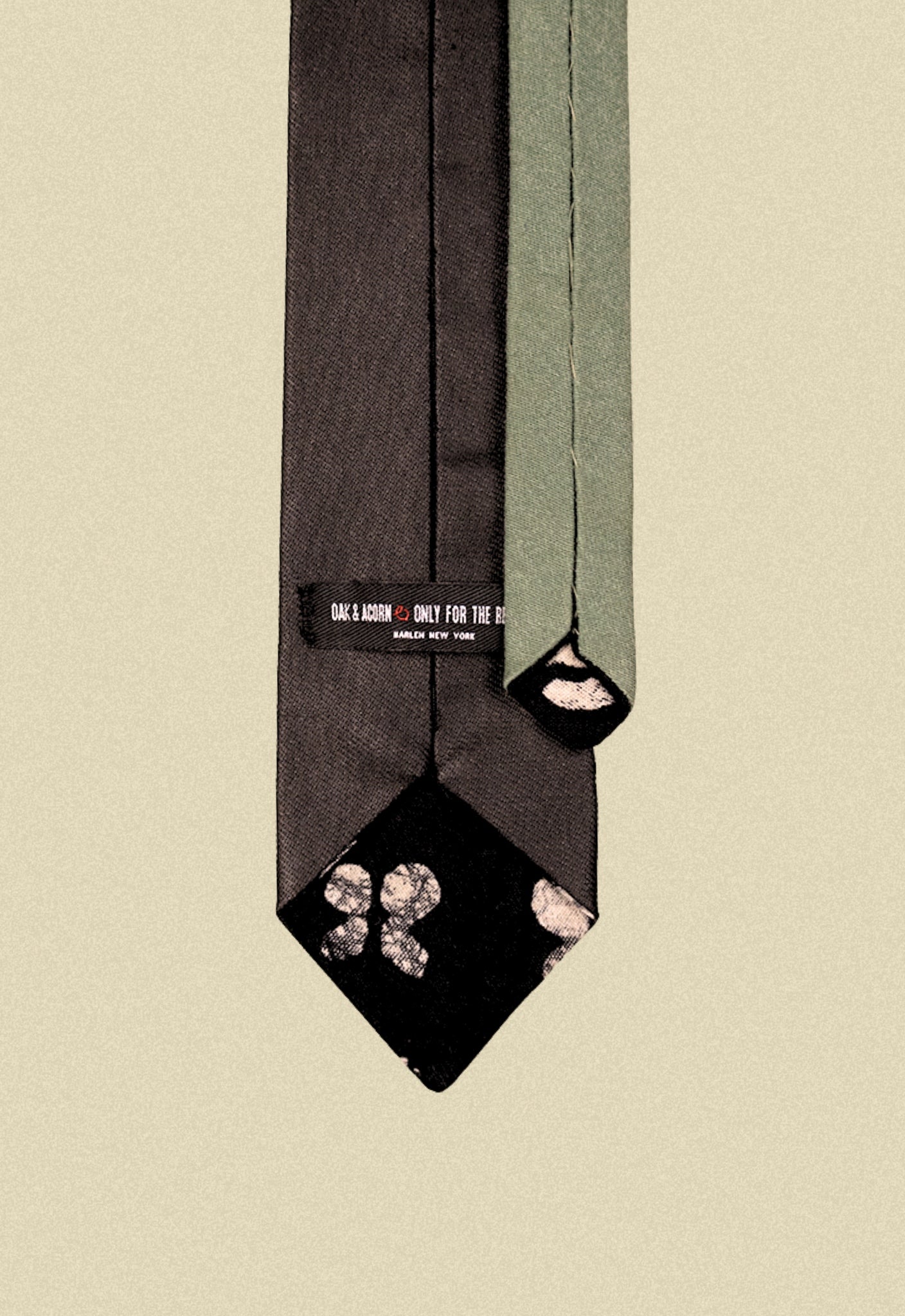 Repurposed coated black and army sateen tie with black sun pattern print fabric detail on a beige background